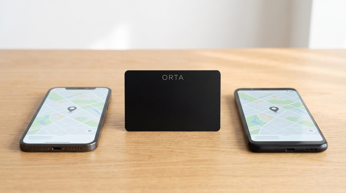 Schwarze ORTA Tracker-Karte zwischen einem iPhone und einem Android-Smartphone mit Kartenansicht auf einem Holztisch